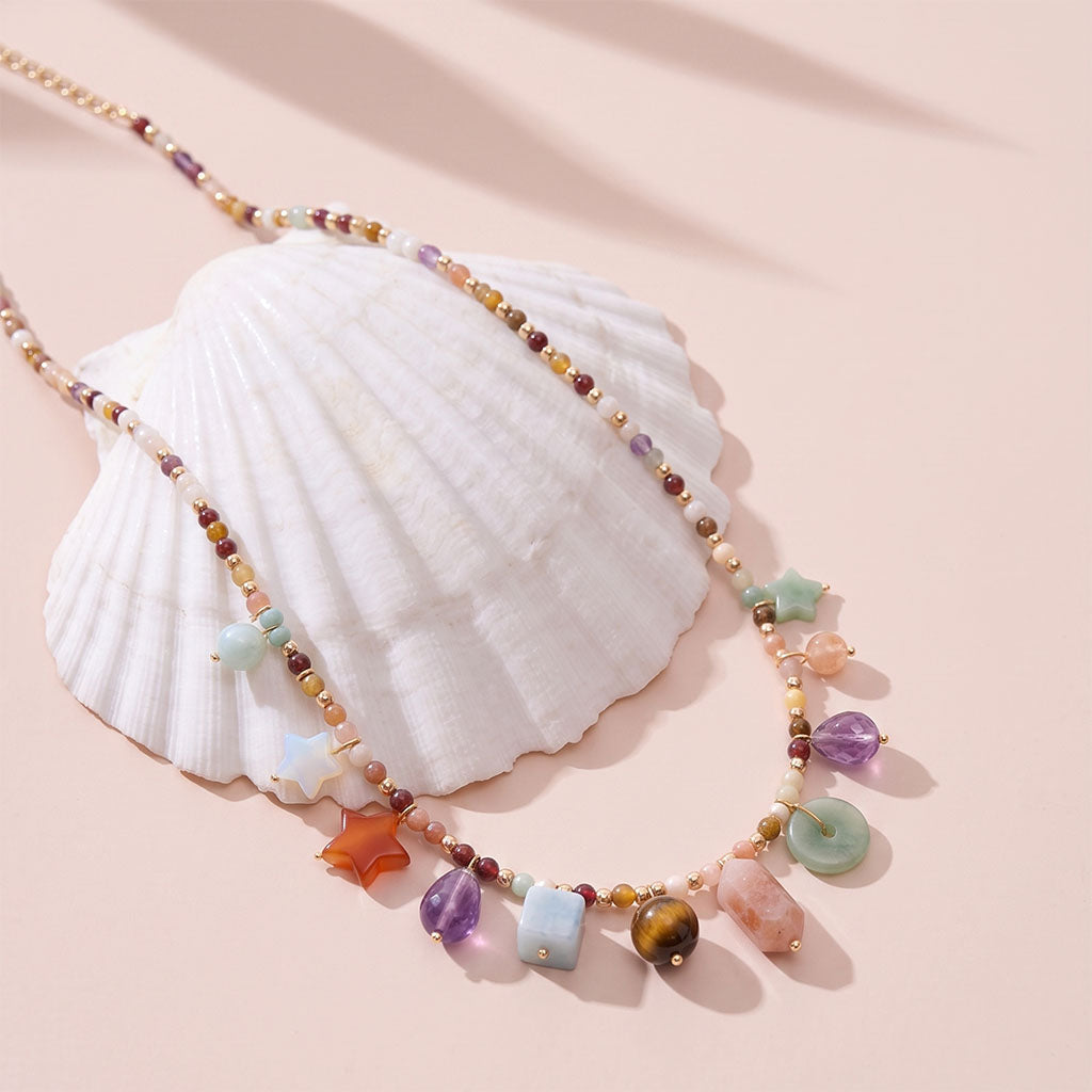 The Celestial Crystal Charm Necklace is displayed on a white seashell, showcasing its details.