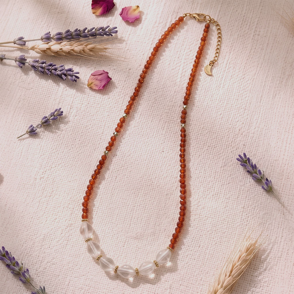 Garnet & Clear Quartz Energy Necklace displayed with natural dried flowers in an elegant flat lay composition